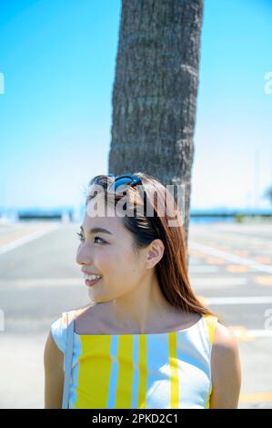 Eine Frau, die in ein Seebad reist und sich gegen eine Palme lehnt Stockfoto