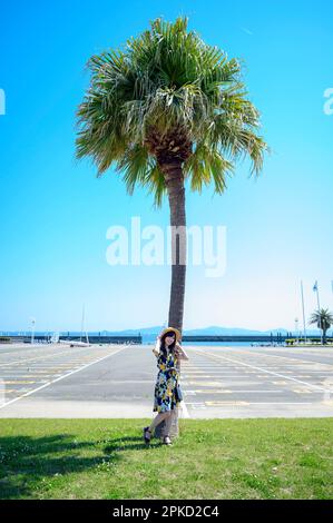 Eine Frau, die zum Seebad reist und sich gegen eine Palme lehnt Stockfoto