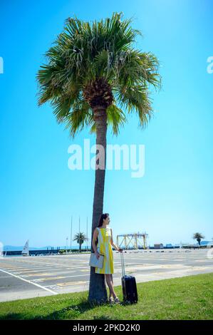 Eine Frau, die in ein Seebad reist und sich gegen eine Palme lehnt Stockfoto