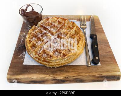 Belgische Waffeln mit Puderzucker, Nutella-Schokoladencreme, Besteck, auf Holzbrett, Stuttgart, Baden-Württemberg, Deutschland Stockfoto