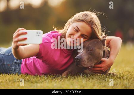 Selfie machen. Eine Frau in lässiger Kleidung ist draußen mit einem Pitbull Stockfoto