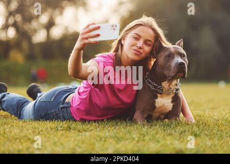 Selfie machen. Eine Frau in lässiger Kleidung ist draußen mit einem Pitbull Stockfoto