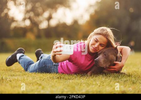 Selfie machen. Eine Frau in lässiger Kleidung ist draußen mit einem Pitbull Stockfoto