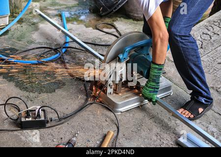 Ein Arbeiter verwendet einen Stahlschneider, um eine große Anzahl von Funken zu erzeugen. Und wenn verschiedene Werkzeuge unvorsichtig in der Nähe einer Wasserquelle platziert werden, kann dies zu einem kurzen Zirkus führen Stockfoto