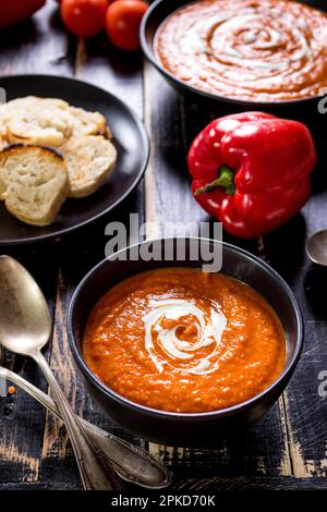 Köstliche Kürbissuppe mit Sahne auf dunklen rustikalen Holztisch mit Red Paprika, Brot, Toast, Linsen, Tomaten Stockfoto