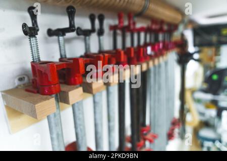 Gruppe von Schienenklemmen für die Holzbearbeitung zum Zusammenkleben von Teilen. Zimmermannsstudio-Interieur. Nahaufnahme im Innenbereich. . Hochwertiges Foto Stockfoto