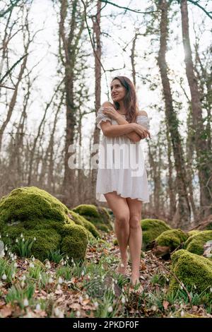 Schneeglöckchen galanthus-Frau. Sie steht in einem weißen Kleid auf einer Wiese mit Schneeglöckchen in einem Frühlingswald Stockfoto