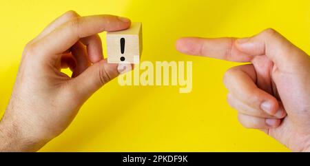 Ein Ausrufezeichen auf einem Holzblock, das ein Mann in der Hand hält und mit dem Zeigefinger auf das Zeichen zeigt Stockfoto