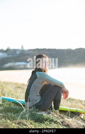 Eine Frau im Neoprenanzug, die am Strand sitzt Stockfoto