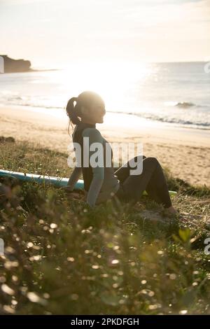 Eine Frau im Neoprenanzug, die am Strand sitzt Stockfoto