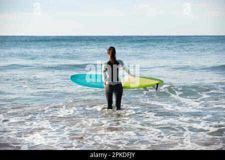 Frau in Neoprenanzug, die mit Surfbrett ins Meer kommt Stockfoto