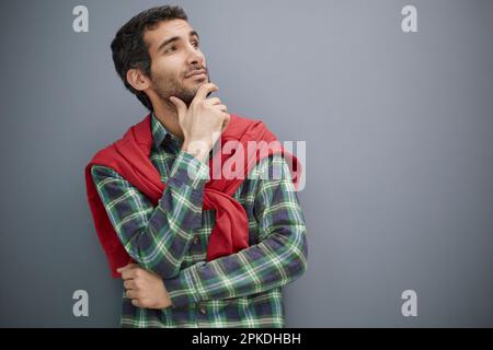 Rücksichtsvoller junger Mann, der auf grauem Hintergrund wegschaut Stockfoto