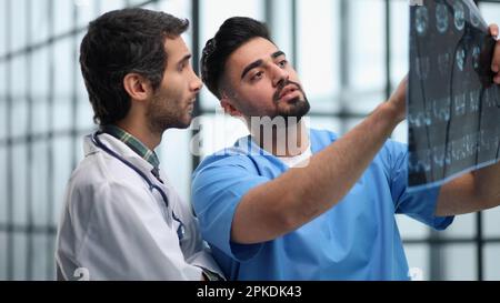 Ärzte und ein Praktikant untersuchen eine Röntgenaufnahme eines Patienten. MRT-Scans von Hirnaktivität und Wissenschaftlern. Stockfoto