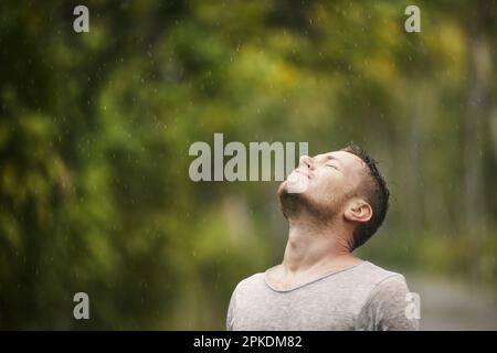 Porträt des Menschen in nassen Kleidern mit geschlossenen Augen bei starkem Regen in der Natur. Themen des Lebens Wasser, Wetter und Umwelt. Stockfoto