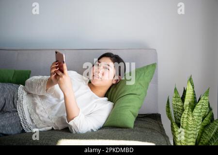 Frau, die ein Smartphone bedient, während sie auf dem Sofa liegt Stockfoto