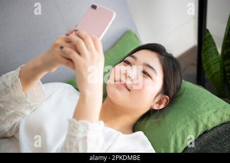 Frau, die ein Smartphone bedient, während sie auf dem Sofa liegt Stockfoto