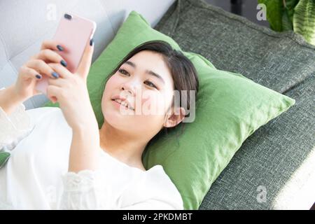 Frau, die ein Smartphone bedient, während sie auf dem Sofa liegt Stockfoto