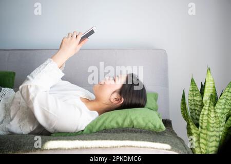 Frau, die ein Smartphone bedient, während sie auf dem Sofa liegt Stockfoto