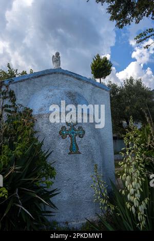 Blaue Kapelle mit Kreuz, in einem Garten an der Küste. Weißer Engel auf dem Dach. Blühender Yucca. Blauer Himmel mit weißen Wolken. Kinira, Thassos (Tassos) isla Stockfoto