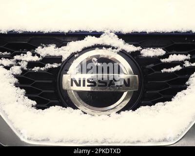 Vorderseite eines Nissan-Autos, mit Schnee bedeckt, mit Markenlogo. Dezember 2022. Stockfoto