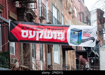 Ein großes Banner, das die Menschen ermutigt, eine Wohltätigkeitsorganisation für satmarische Jeschivas in Israel zu spenden, indem sie Münzen in einen puschka legen. In der Rodney Street in Brooklyn, New York. Stockfoto