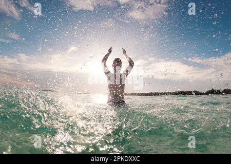 Silhouette eines fröhlichen Mannes, der im Meer steht und Wasser in die Kamera spritzt. Sonniger Tag im tropischen Reiseziel während des Strandurlaubs. Stockfoto