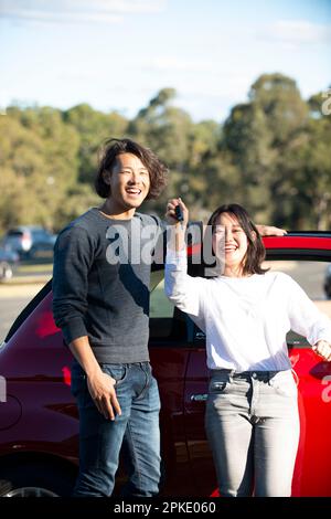 Mann und Frau, die vor dem roten Auto lachen Stockfoto