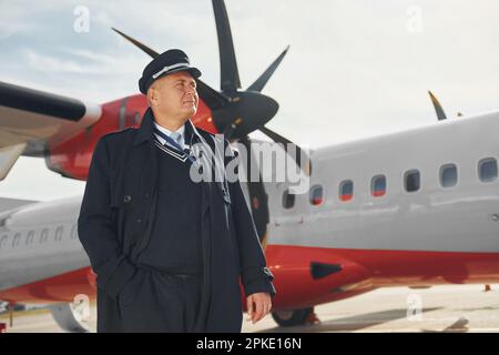 Der Pilot in formeller schwarzer Uniform steht draußen in der Nähe des Flugzeugs Stockfoto