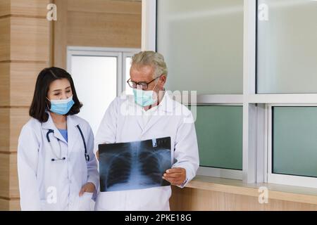 Expertise Senior Chirurgie schaut auf Röntgenfilm, um Beratung und Diskussion für die chirurgische Behandlung der Patient mit junger asiatischer Ärztin in Hospita Stockfoto