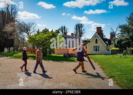 Thaxted, England, Gb 07. April 2023. Thaxted Essex UK Zeugenprozession am Karfreitag 7. April 2023 Daniel Fox trägt das christliche Kreuz der Opfer, während er die Prozession am Osterfreitagmorgen durch die wunderschöne Stadt Thaxted im Nordwesten von Essex führt. Hier mit Thaxted Alms House und Chantry und Hohn Webbs Windmill im Hintergrund. Kredit: BRIAN HARRIS/Alamy Live News Stockfoto