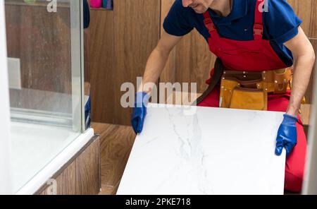 Ein männlicher Bauarbeiter installiert eine große Keramikfliese Stockfoto