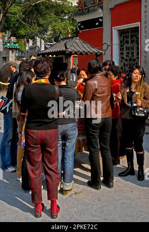 Auf dem Gelände des A-Ma-Tempels in Macau, China, beten die Gläubigen leichte Handvoll Joss-Sticks auf einer Sandbank oder unter einem traditionellen Dach, mit nach oben gedrehten Ecken und schmiedeeisernen Finalen. Der Tempel, gewidmet der taoistischen Muttergöttin A-Ma oder Tin Hau, Beschützerin der Seeleute, stammt aus dem Jahr 1488 n. Chr. und wurde an der Stelle erbaut, an der sie angeblich nach einem Schiffswrack gelandet ist. Stockfoto