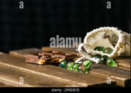 Bild von Glasmarmor für Kinderspiele und eine Schokoladentablette mit Haselnüssen auf einem Holztisch Stockfoto