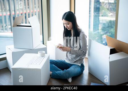 Eine Frau, die ihr Handy berührt, umgeben von sich bewegendem Pappe Stockfoto