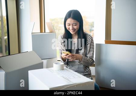 Frau, die ihr Smartphone berührt, umgeben von sich bewegendem Karton Stockfoto