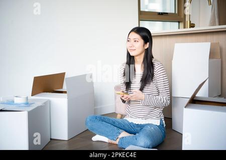 Frau, die ihr Smartphone berührt, umgeben von sich bewegendem Karton Stockfoto