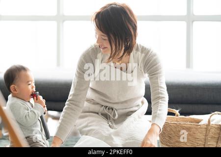 Mutter und Baby lachen, während sie Wäsche zusammenlegen Stockfoto