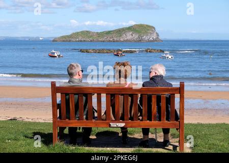 North Berwick, Schottland, Großbritannien. 07. April 2023 Ein herrlicher, sonniger Start in den Morgen bringt Osterurlauber-Besucher und Einheimische an die Strände von North Berwick. Sie sitzen auf einer Bank mit Blick auf West Bay Beach und Craigleith. Kredit: Craig Brown/Alamy Live News Stockfoto