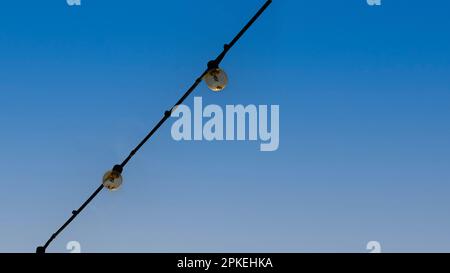 Eine Gruppe von Glühbirnen, die an Drähten hängen, gegen die am blauen Himmel hing. Stockfoto