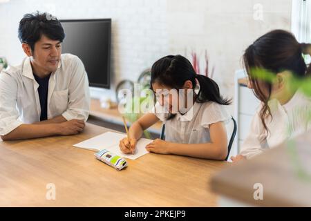 Ein Mädchen aus der Grundschule, das studiert, und ihre Eltern passen auf sie auf Stockfoto