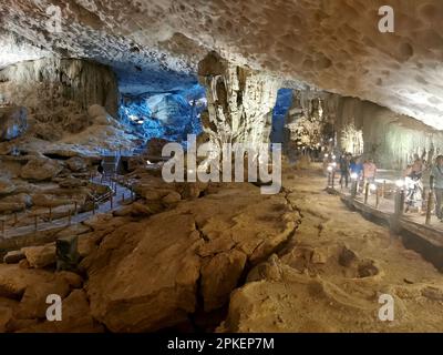 28. Februar 2023, Vietnam, Halong-Bucht: Besucher spazieren durch die Überraschungshöhle (Hang Sung Sot). Die Höhle Sung Sot befindet sich auf der Insel Bo Hòn und wurde erstmals 1901 von französischen Entdeckern entdeckt. Die riesige Höhle erstreckt sich über eine Fläche von mehr als 12.200 Quadratmetern und besteht aus drei kleineren Abteilungen oder „Räumen“, die jeweils mit beeindruckenden Stalaktiten gefüllt sind. Die Halong-Bucht (vietnamesisch: Vinh Ha Long) ist eine Fläche von etwa 1.500 Quadratkilometern im Golf von Tonkin in der Provinz Quang Ninh im Norden Vietnams. 1994 wurde die Bucht von der UNESCO zum Weltkulturerbe erklärt. Foto: Alexandra Schuler/dpa Stockfoto