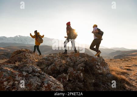 Eine Gruppe junger Wanderer wandert bei Sonnenuntergang in den Bergen. Silhouetten von Wandertouristen mit Rucksäcken Stockfoto