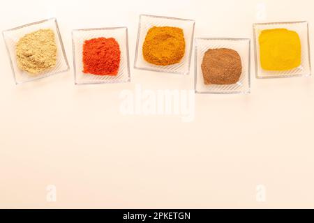 Verschiedene getrocknete Gewürze in kleinen Schüsseln auf beigefarbenem Tisch. Flach liegend mit Kopierbereich Stockfoto
