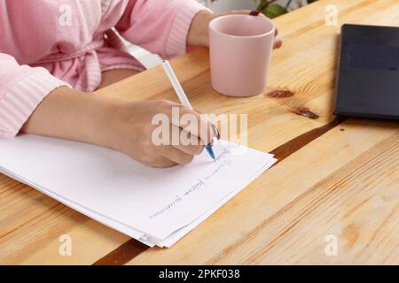 Eine Frau im Bademantel isst nach der Dusche im Heimbüro ein köstliches Dessert zum Frühstück. Eine Frau mittleren Alters arbeitet zu Hause an einem Computer in der Küche. Stockfoto