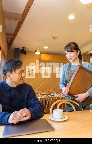 Weibliche Kellnerin, die einem männlichen Gast Kaffee serviert Stockfoto