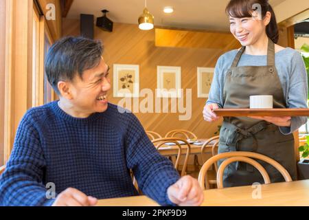 Weibliche Kellnerin, die einem männlichen Gast Kaffee serviert Stockfoto