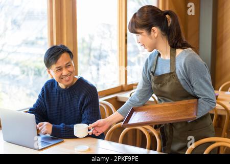 Weibliche Kellnerin, die einem männlichen Gast Kaffee serviert Stockfoto