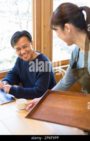 Weibliche Kellnerin, die einem männlichen Gast Kaffee serviert Stockfoto