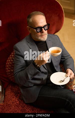 Ein erwachsener Mann sitzt in einem luxuriösen Sessel aus Samt Stockfoto
