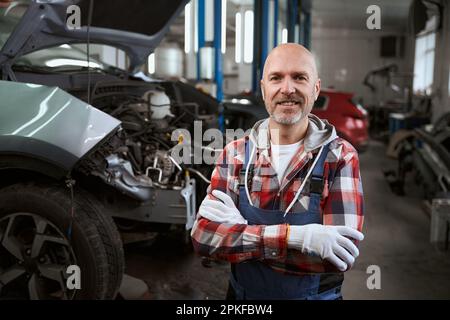 Ein lächelnder Autohersteller steht vor dem Hintergrund von Autos an seinem Arbeitsplatz Stockfoto